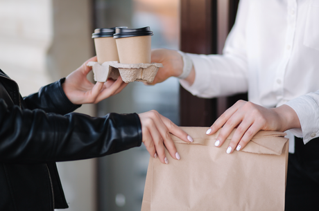 Customer stands outdoors at a takeout window, receiving a coffee and food package from a cashier in winter