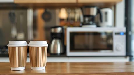 2 coffee cups sitting on kitchen island with microwave oven and kettle in the background.