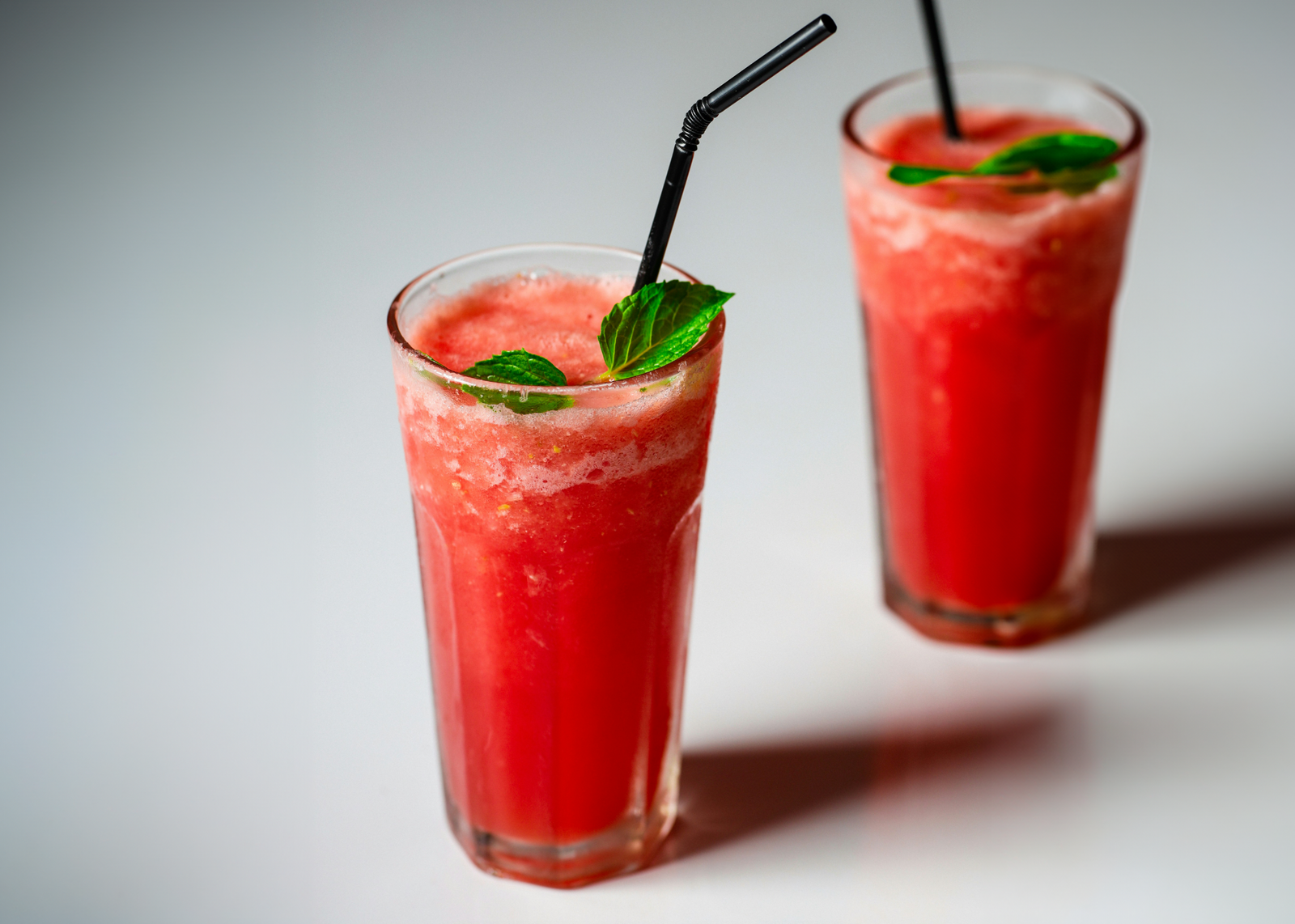 2 glasses of watermelon mint cooler drink with mint leaves and black straw