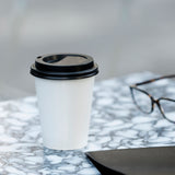 a white coffee paper cup on a table with a pair glasses and file binder beside.