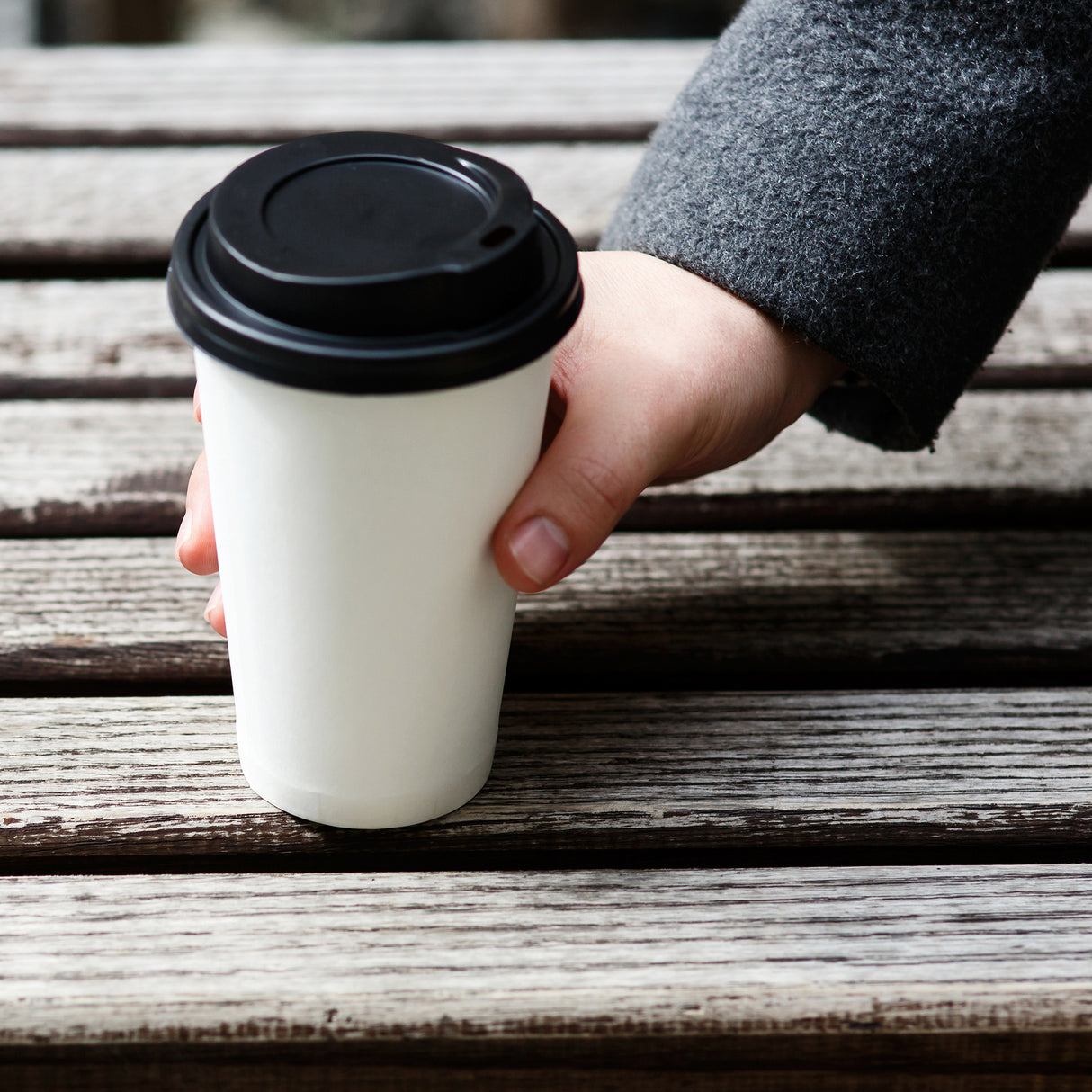 a person is holding a white paper coffee cup with black sip lid