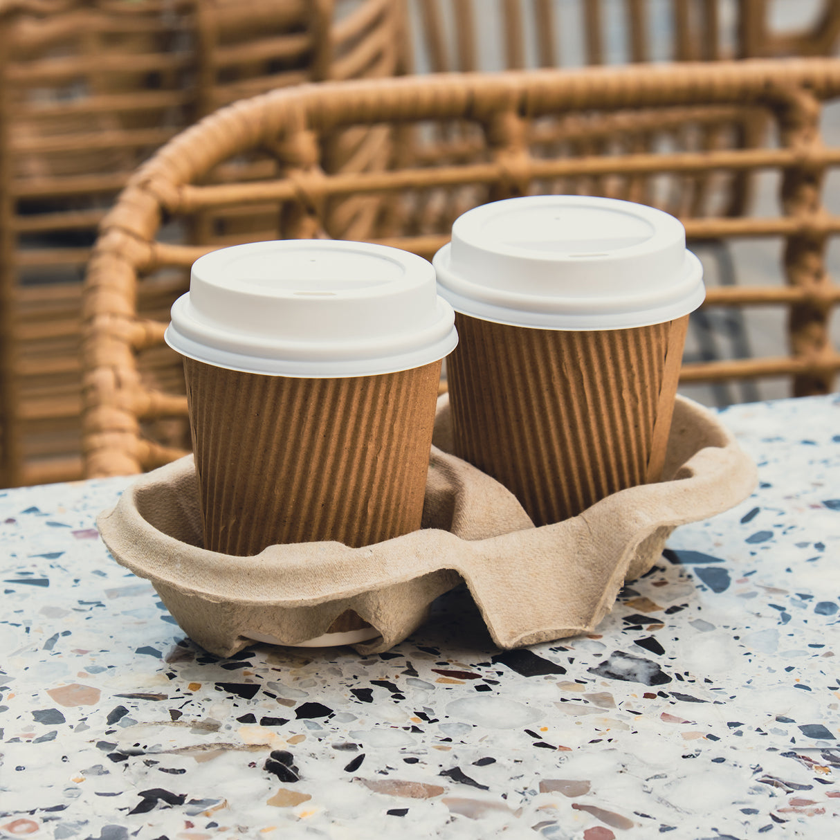 2 double wall coffee cups with white lids sitting in a pulp cup tray