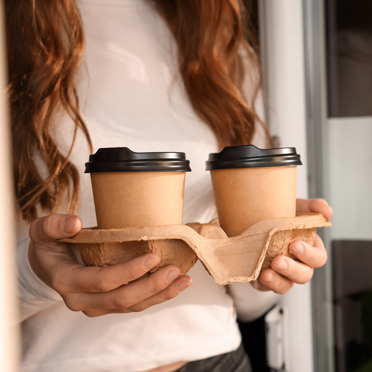 a female is holding 2 coffee cups in a tray