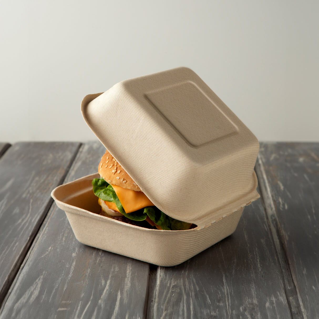 compostable sugarcane clamshell container in natural colour that has a cheeseburger inside.