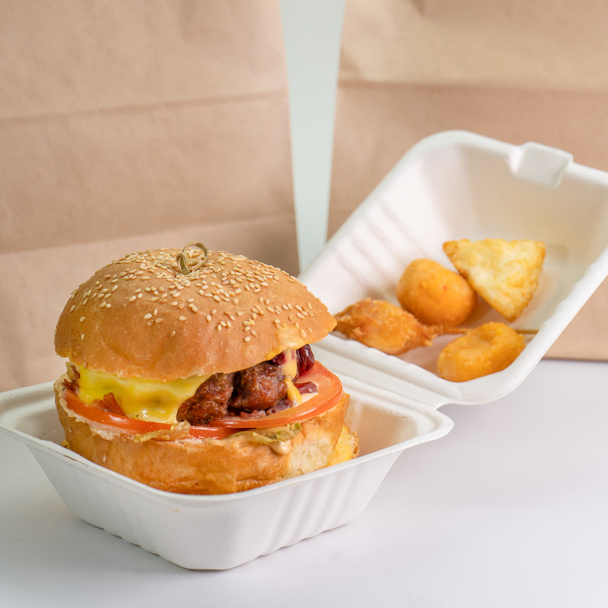 cheeseburger and fried potato wedges sitting in white bagasse clamshell