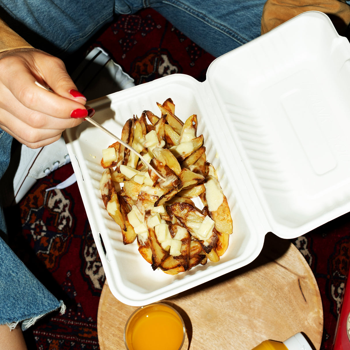 a person wearing jeans is holding white sugarcane food box with poutine inside.