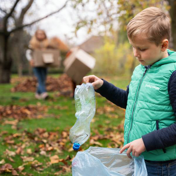 a little boy wearing green pakpakgo vest picking up plastic waste to recycle