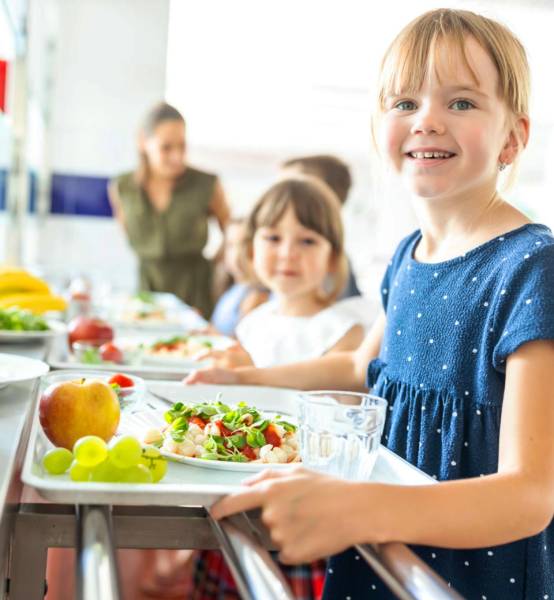 a white young kid holding her food tray at school during lunch.