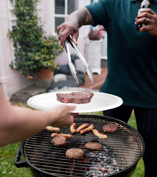 a black male is handing over a piece of steak placing it onto a bagasse plate during a home party BBQ event