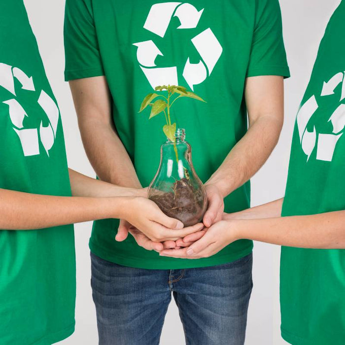 3 people wearing green t-shirts with recycle logo holding a plant.