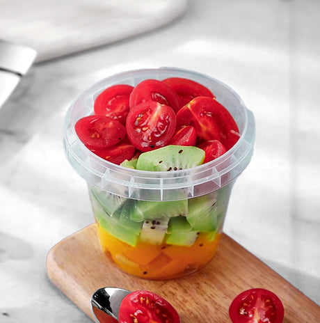 plastic deli container with cherry tomato, kiwi on a cutting board.