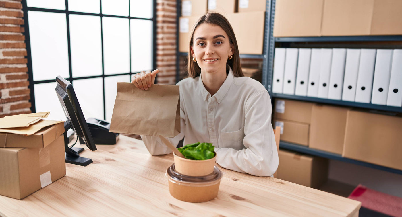 an office girl holding paper bag with two salad bowls on the desk for lunch