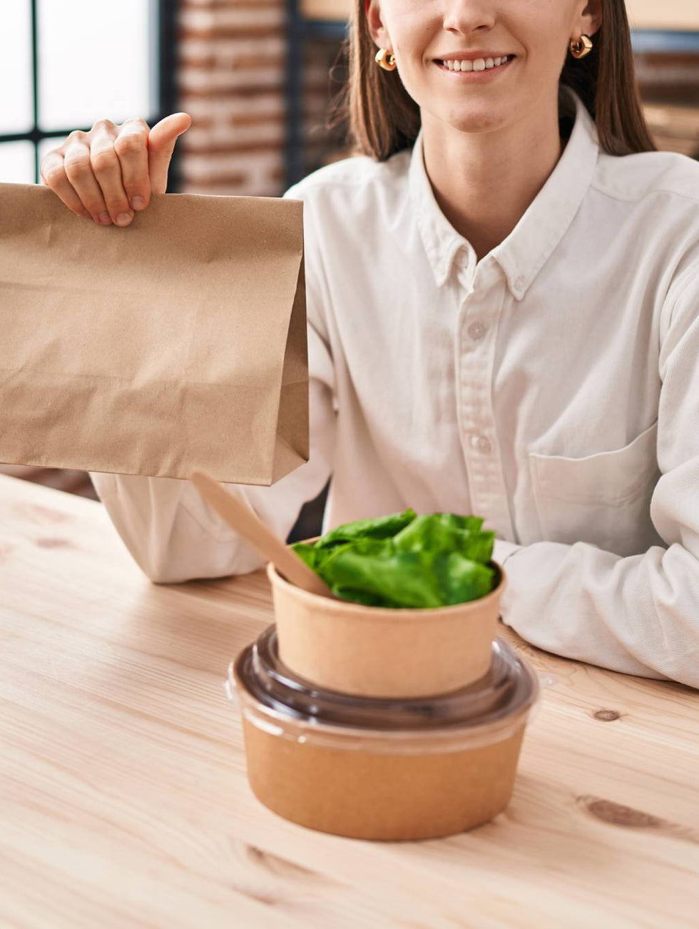 an office girl holding paper bag with two salad bowls on the desk for lunch