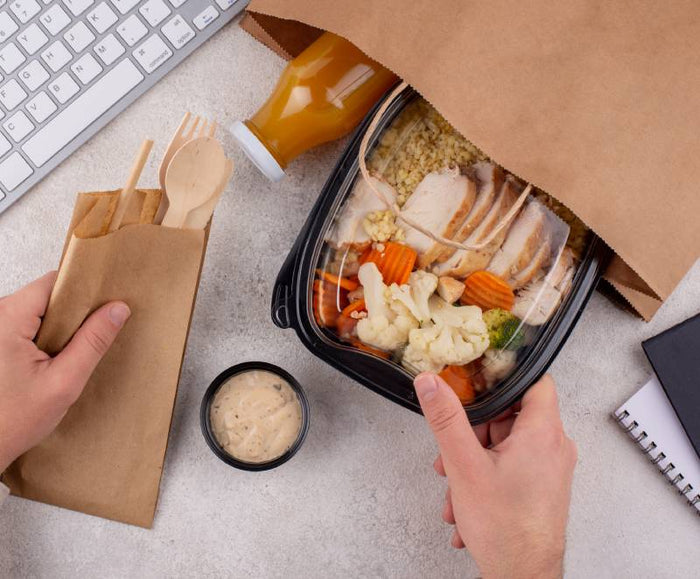 a person is taking out lunch packed in plastic food container from paper bag for lunch in the office